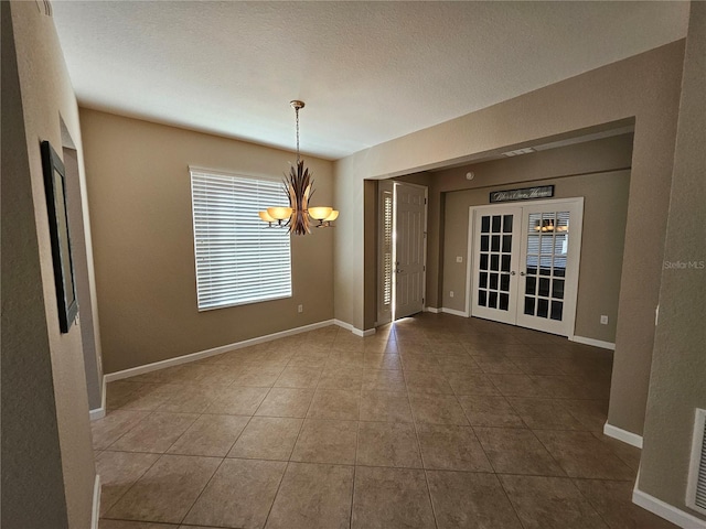 unfurnished dining area with tile patterned flooring, a chandelier, a textured ceiling, and french doors