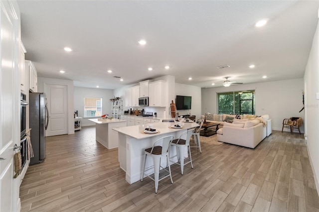 kitchen with appliances with stainless steel finishes, white cabinetry, an island with sink, a kitchen breakfast bar, and light wood-type flooring