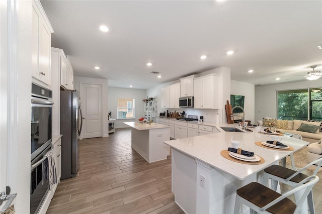 kitchen with a kitchen island, kitchen peninsula, a kitchen bar, stainless steel appliances, and white cabinets