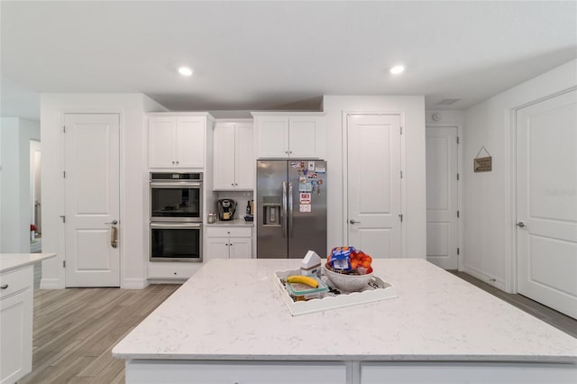 kitchen with white cabinetry, appliances with stainless steel finishes, light wood-type flooring, light stone countertops, and a kitchen island