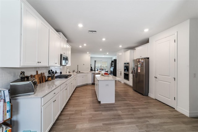 kitchen with light hardwood / wood-style floors, a center island, kitchen peninsula, white cabinetry, and stainless steel appliances