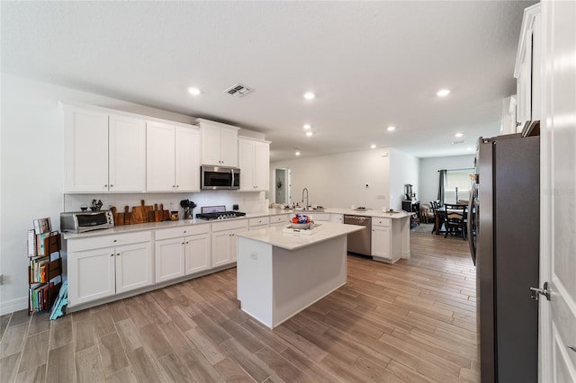 kitchen with white cabinets, kitchen peninsula, stainless steel appliances, and a center island