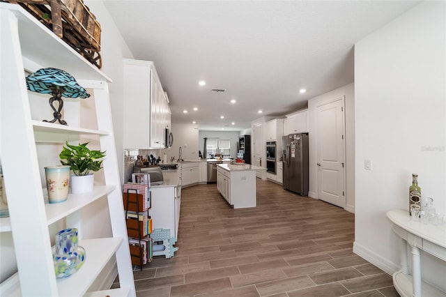 kitchen with appliances with stainless steel finishes, a kitchen island, white cabinetry, sink, and kitchen peninsula