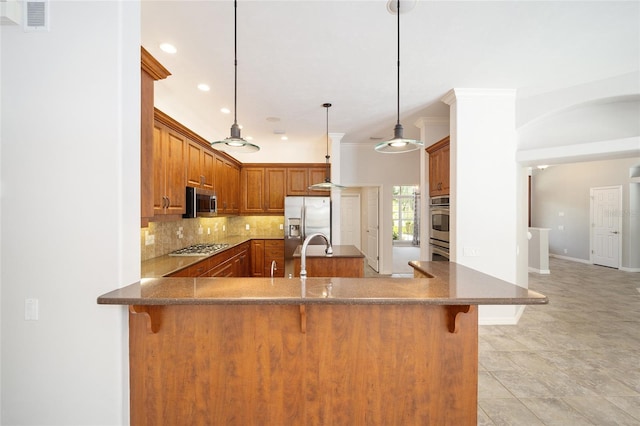 kitchen featuring a breakfast bar area, a peninsula, appliances with stainless steel finishes, backsplash, and brown cabinetry