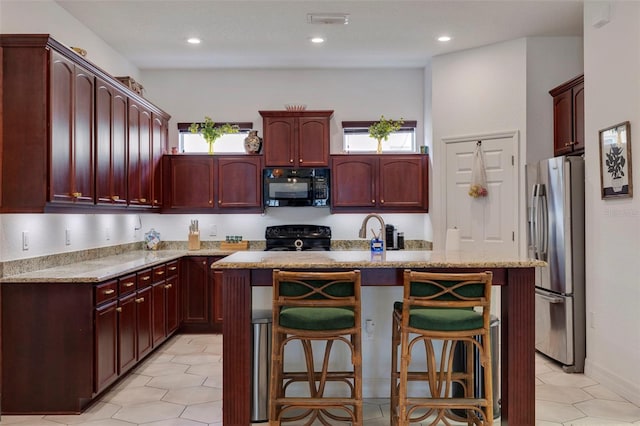 kitchen featuring a breakfast bar, a wealth of natural light, a center island with sink, and black appliances