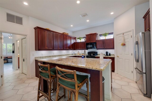 kitchen featuring black appliances, a kitchen island, light stone counters, and a breakfast bar area