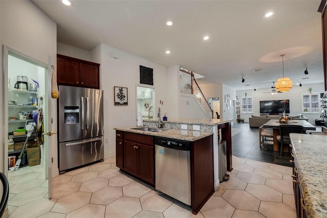 kitchen featuring light stone countertops, stainless steel appliances, ceiling fan, sink, and a center island with sink