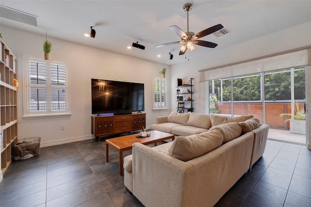 living room with a textured ceiling, ceiling fan, and dark tile patterned flooring