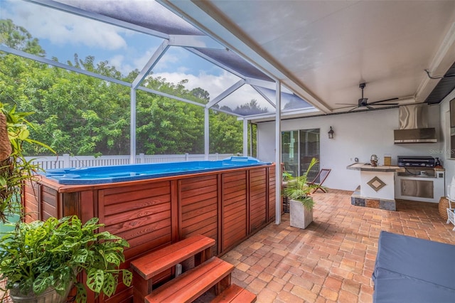 view of patio with glass enclosure, ceiling fan, an outdoor kitchen, and a pool