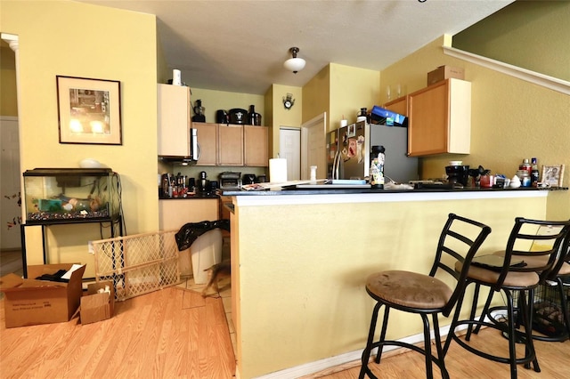 kitchen with stainless steel refrigerator, light wood-type flooring, and a kitchen bar