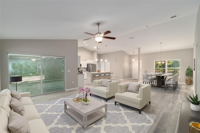 living room with ceiling fan, vaulted ceiling, and light hardwood / wood-style flooring