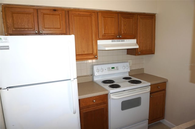 kitchen featuring brown cabinets, under cabinet range hood, white appliances, and decorative backsplash