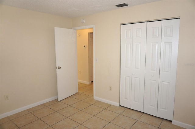 unfurnished bedroom featuring a textured ceiling, light tile patterned flooring, visible vents, baseboards, and a closet