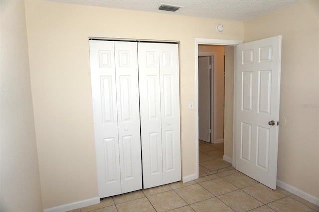 unfurnished bedroom with light tile patterned floors, a closet, visible vents, a textured ceiling, and baseboards