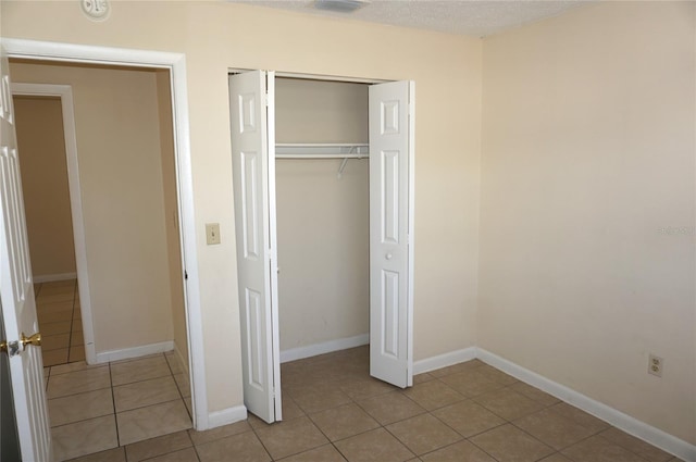 unfurnished bedroom with a closet, a textured ceiling, baseboards, and light tile patterned floors