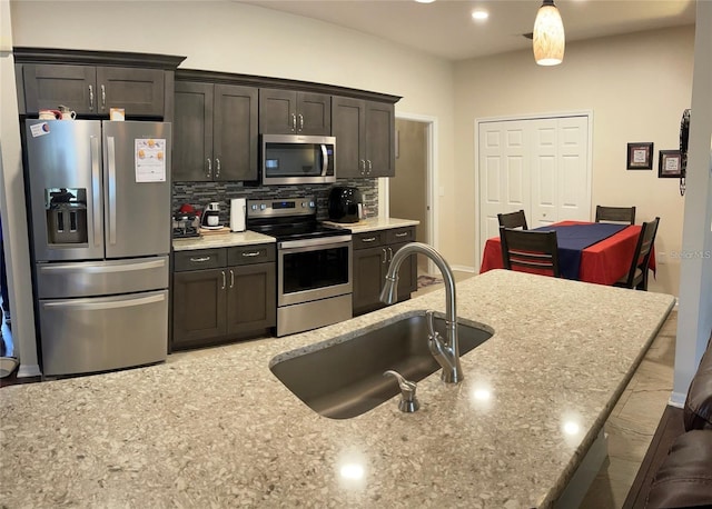 kitchen with decorative backsplash, sink, stainless steel appliances, dark brown cabinets, and light stone counters