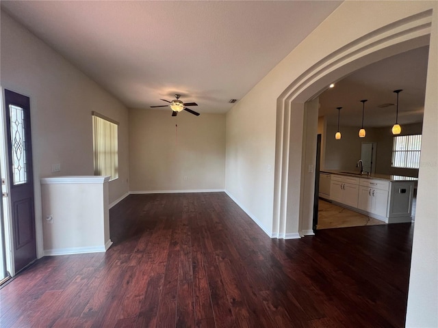 unfurnished room featuring a sink, a ceiling fan, wood finished floors, arched walkways, and baseboards