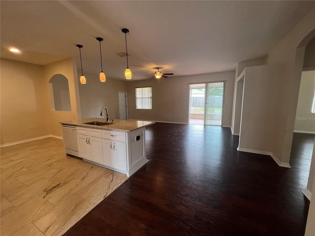 kitchen with arched walkways, white dishwasher, open floor plan, a sink, and a ceiling fan