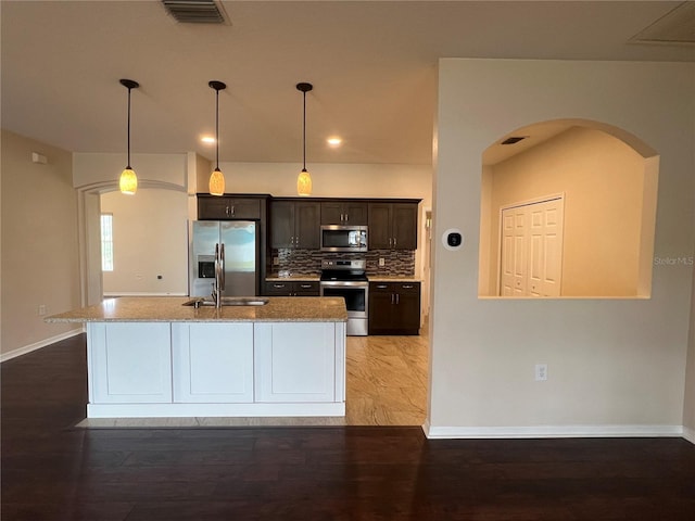 kitchen featuring appliances with stainless steel finishes, arched walkways, baseboards, tasteful backsplash, and light wood-type flooring