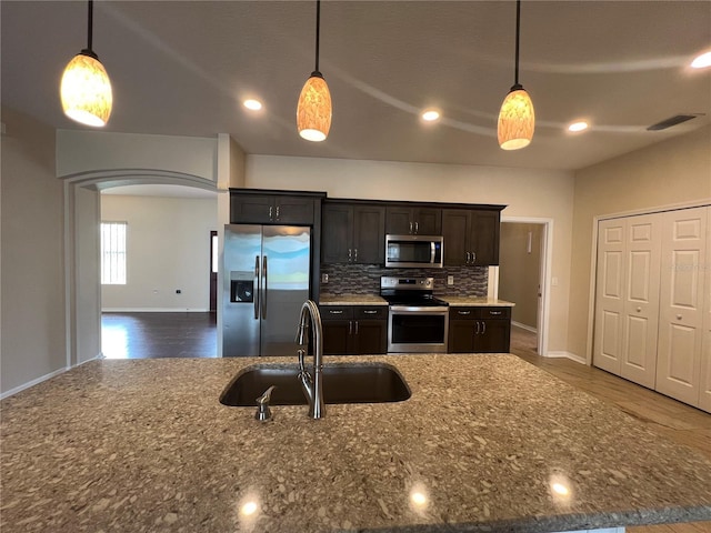 kitchen with stainless steel appliances, a sink, arched walkways, baseboards, and dark stone counters