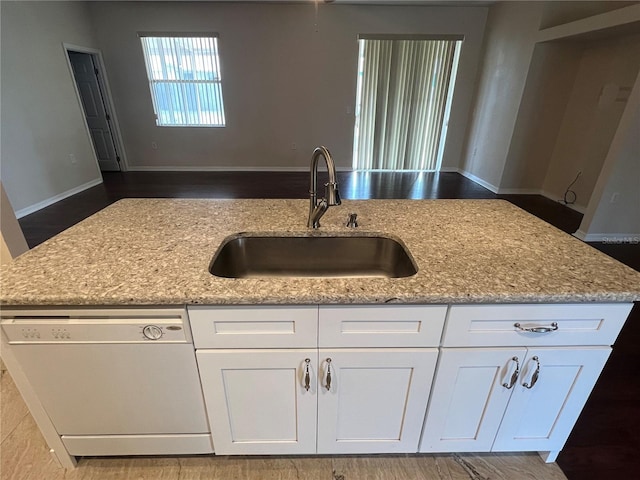 kitchen featuring dishwasher, a sink, light stone counters, open floor plan, and white cabinets