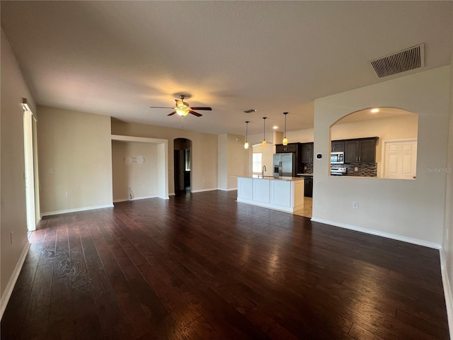 unfurnished living room featuring arched walkways, a ceiling fan, hardwood / wood-style floors, and baseboards