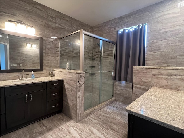 full bathroom with tile walls, a shower stall, vanity, and marble finish floors