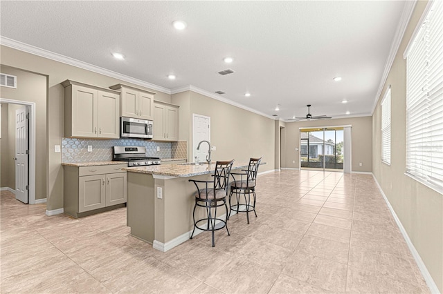 kitchen featuring gray cabinetry, light stone counters, a center island with sink, appliances with stainless steel finishes, and a kitchen breakfast bar