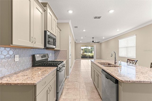 kitchen with light tile patterned flooring, sink, appliances with stainless steel finishes, light stone countertops, and a kitchen island with sink