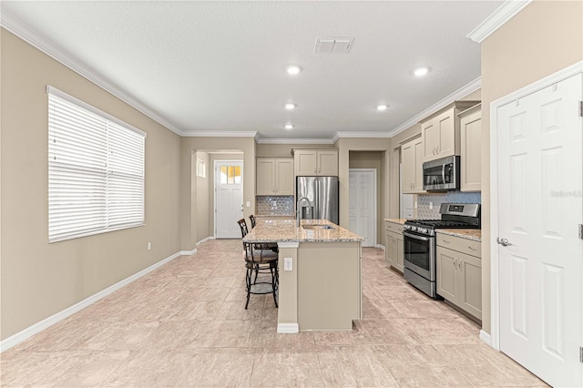 kitchen featuring a breakfast bar, a center island with sink, appliances with stainless steel finishes, light stone countertops, and backsplash