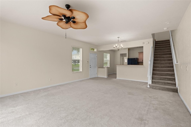 unfurnished living room featuring ceiling fan with notable chandelier and light colored carpet