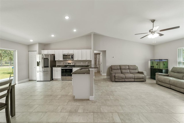 kitchen with appliances with stainless steel finishes, sink, white cabinetry, dark stone counters, and lofted ceiling