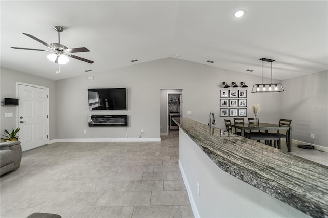 interior space with vaulted ceiling, dark stone countertops, ceiling fan, and pendant lighting