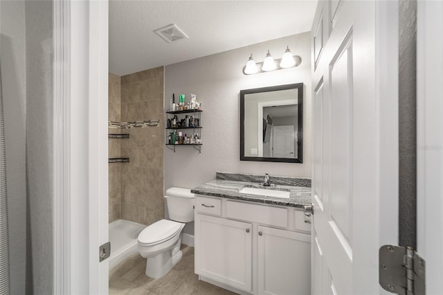 bathroom with a textured ceiling, toilet, vanity, and a tile shower