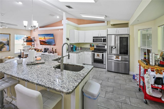 kitchen with a breakfast bar area, vaulted ceiling, stainless steel appliances, sink, and white cabinets