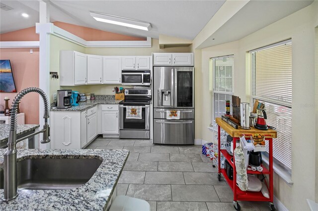 kitchen with appliances with stainless steel finishes, sink, white cabinetry, and vaulted ceiling