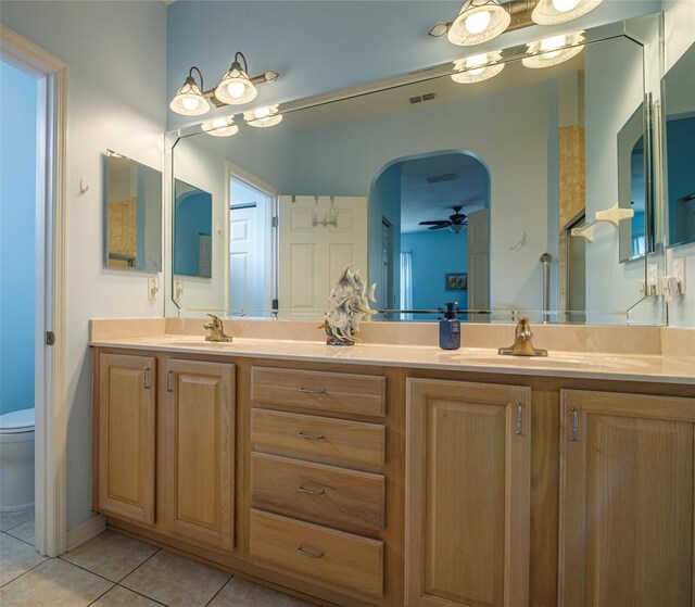 bathroom with tile patterned flooring, ceiling fan with notable chandelier, toilet, and dual bowl vanity