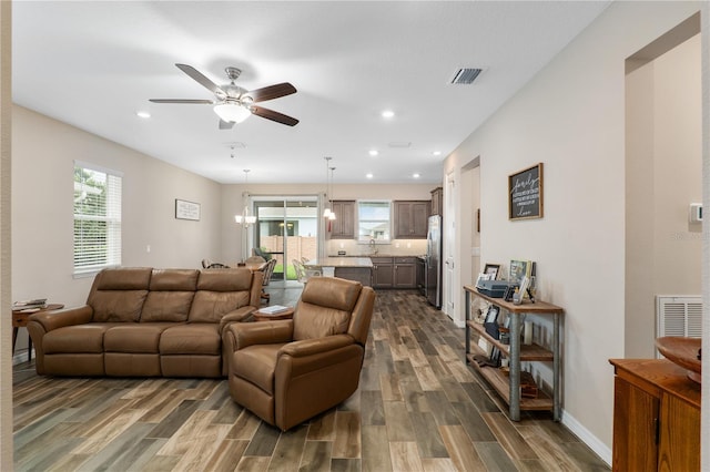 living room with ceiling fan with notable chandelier and dark wood-type flooring