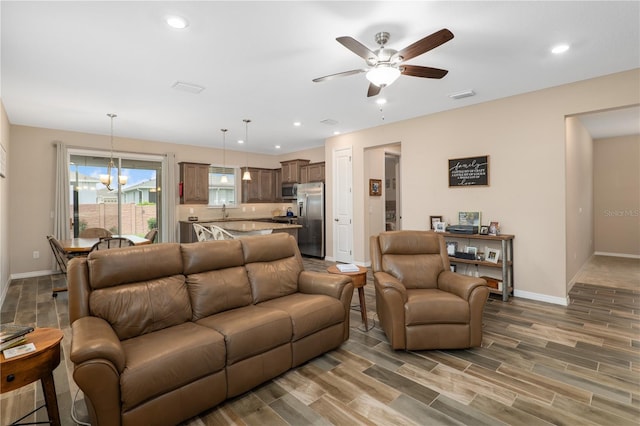 living room featuring ceiling fan with notable chandelier, sink, and wood-type flooring