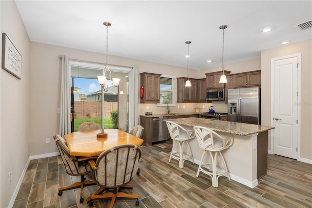 kitchen featuring appliances with stainless steel finishes, decorative light fixtures, light stone countertops, a center island, and decorative backsplash