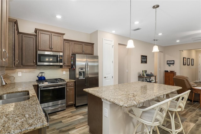 kitchen with appliances with stainless steel finishes, hanging light fixtures, sink, a kitchen island, and dark hardwood / wood-style floors