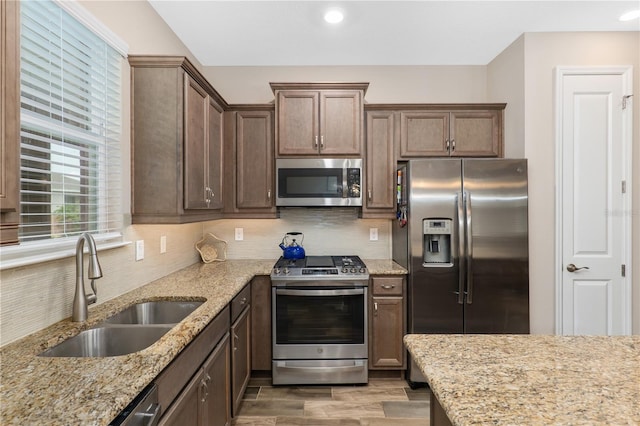 kitchen with light stone countertops, appliances with stainless steel finishes, tasteful backsplash, wood-type flooring, and sink