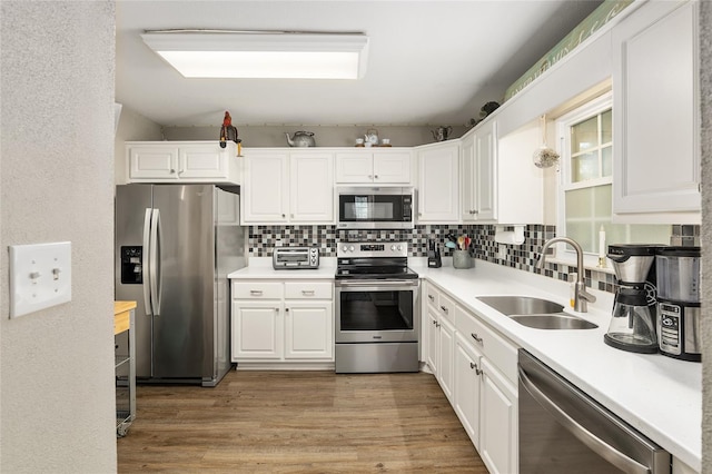 kitchen with appliances with stainless steel finishes, white cabinetry, sink, decorative backsplash, and light hardwood / wood-style floors