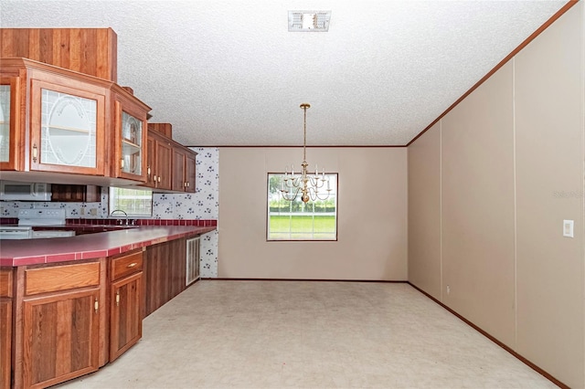 kitchen featuring white electric range, a chandelier, a textured ceiling, ornamental molding, and pendant lighting