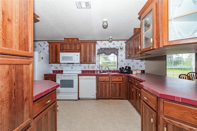 kitchen with light floors, dark countertops, glass insert cabinets, white appliances, and wallpapered walls