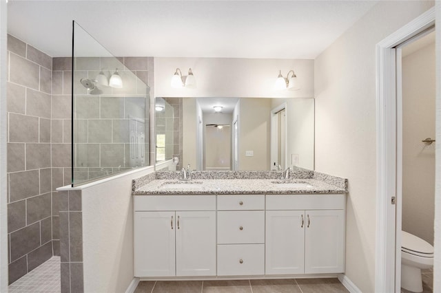 bathroom with tile patterned flooring, a tile shower, toilet, and dual bowl vanity