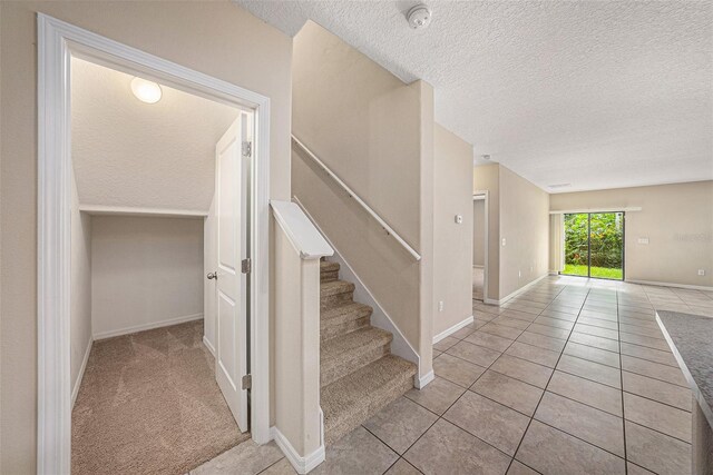 stairway with a textured ceiling and light tile patterned floors