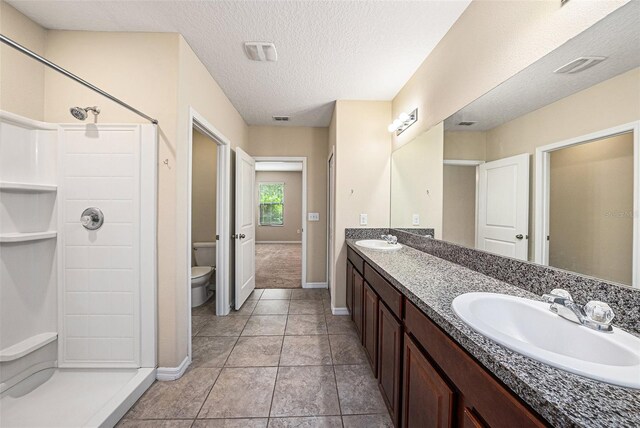 bathroom featuring tile patterned flooring, walk in shower, a textured ceiling, toilet, and dual vanity