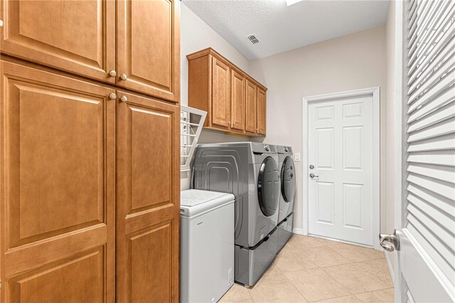 washroom with a textured ceiling, cabinets, washing machine and clothes dryer, and light tile patterned flooring