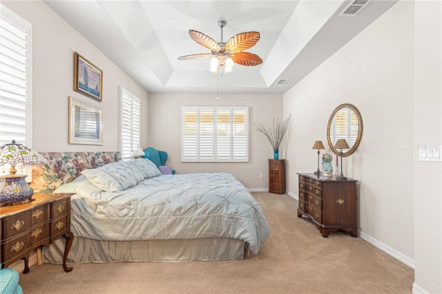 bedroom with a raised ceiling, light carpet, and ceiling fan